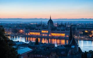 Veduta panoramica del Parlamento di Budapest illuminato di notte riflesso sulle acque del fiume Danubio.