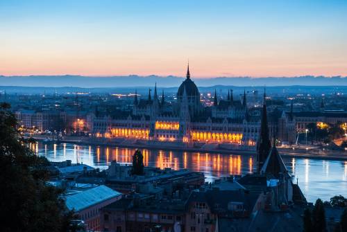 Veduta panoramica del Parlamento di Budapest illuminato di notte riflesso sulle acque del fiume Danubio.